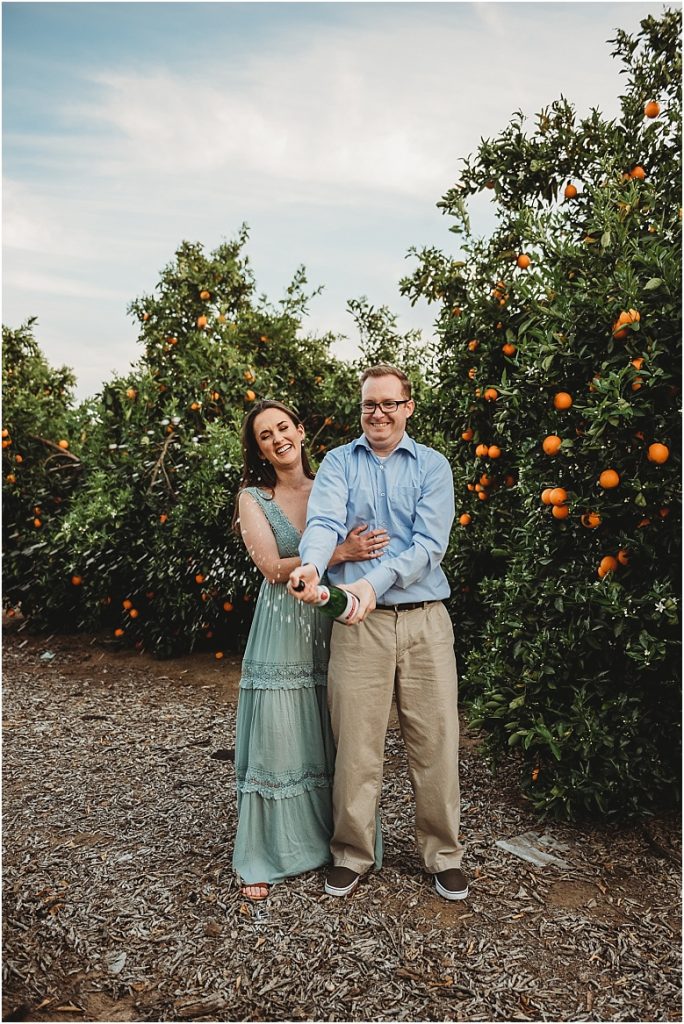 couple popping champagne in orange groves at California Citrus State Historic Park in Riverside, CA by Dallas Wedding Photographer for their engagement session 